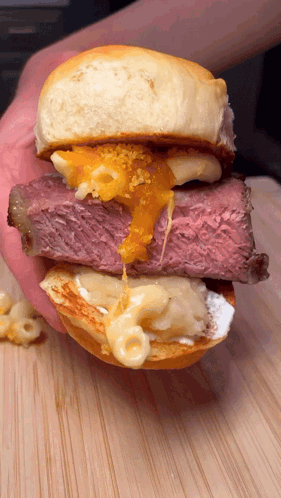 A Close Up Of A Person Holding A Sandwich With Meat And Cheese On A Bun GIF