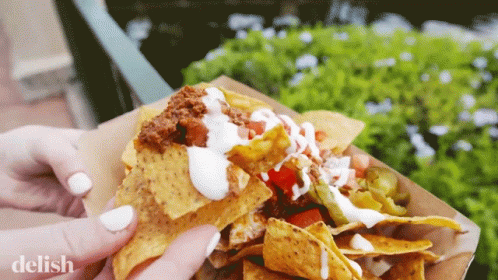 A Close Up Of A Person Holding A Tray Of Nachos With The Word Delish On The Bottom GIF