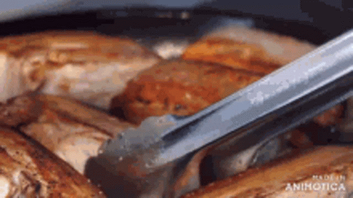 A Close Up Of A Person Holding Tongs Over A Pan Of Meat . GIF