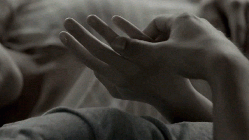 A Close Up Of A Person Laying On A Bed Holding Another Person 'S Hand . GIF