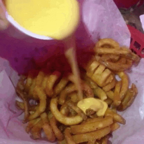 A Close Up Of A Person Pouring Cheese On Curly Fries GIF