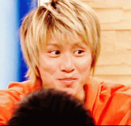 A Close Up Of A Person 'S Face With Blonde Hair And An Orange Shirt GIF