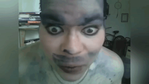 A Close Up Of A Person 'S Face With Books On The Shelf Behind Them GIF