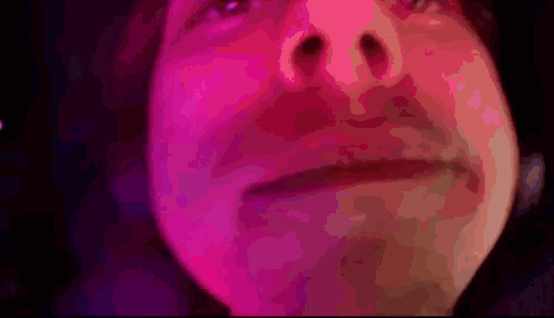 A Close Up Of A Person 'S Face With Pink And Purple Lights Behind Them GIF