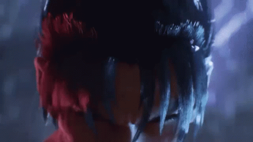 A Close Up Of A Person 'S Face With Red And Black Hair And A Purple Background . GIF