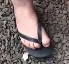 A Close Up Of A Person 'S Foot Wearing A Pair Of Flip Flops On A Pile Of Rocks . GIF