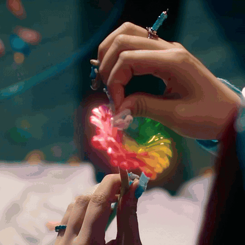 A Close Up Of A Person 'S Hands Holding A Rainbow Colored Flower GIF