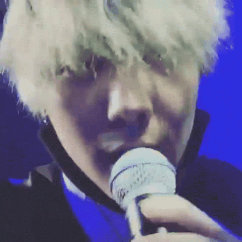 A Close Up Of A Person Singing Into A Microphone With A Blue Background GIF