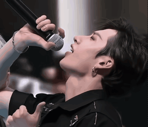 A Close Up Of A Person Singing Into A Microphone With The Letter T On His Shirt GIF