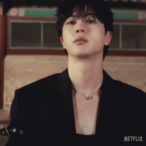 A Close Up Of A Person Wearing A Black Jacket And A Necklace With Netflix Written On The Bottom GIF