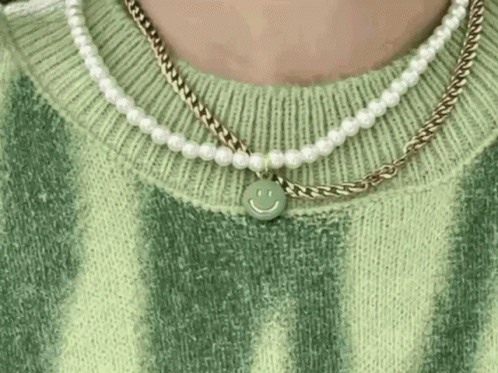 A Close Up Of A Person Wearing A Green Sweater And A Necklace With A Smiley Face Pendant . GIF