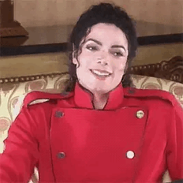 A Close Up Of A Person Wearing A Red Jacket And Smiling While Sitting On A Couch . GIF