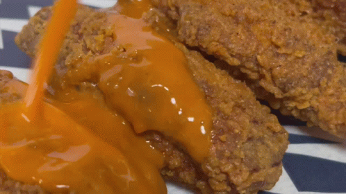 A Close Up Of A Piece Of Fried Chicken Covered In Sauce GIF
