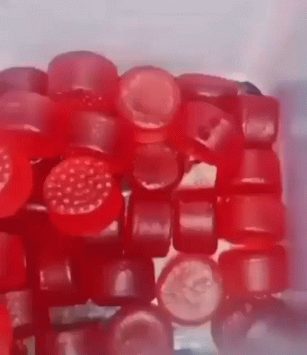 A Close Up Of A Pile Of Red Gummy Bears Sitting On Top Of Each Other On A Table . GIF