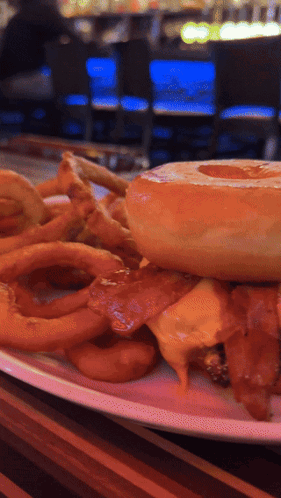 A Close Up Of A Plate Of Food With A Hamburger And Onion Rings GIF