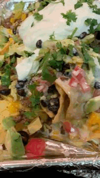 A Close Up Of A Plate Of Nachos With Avocado And Sour Cream On Aluminum Foil GIF