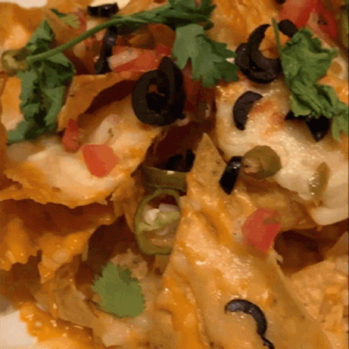 A Close Up Of A Plate Of Nachos With Black Olives And Tomatoes GIF