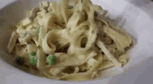 A Close Up Of A Plate Of Pasta With Peas And Chicken In A Sauce . GIF