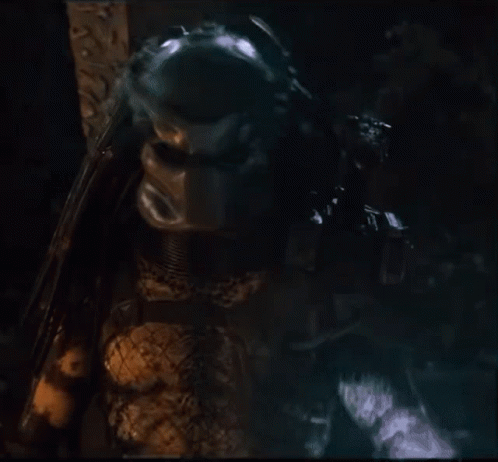 A Close Up Of A Predator Holding A Gun In A Dark Room GIF