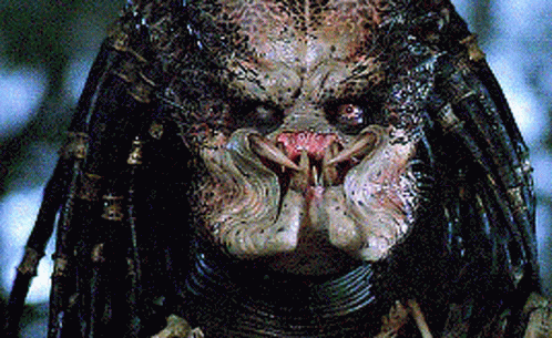 A Close Up Of A Predator 'S Face With Dreadlocks And Sharp Teeth GIF