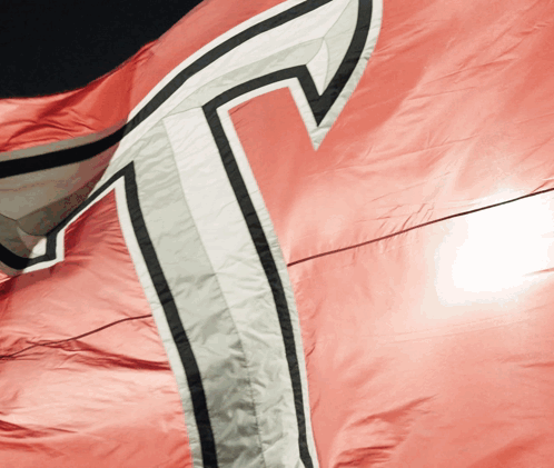 A Close Up Of A Red Flag With A White T On It GIF