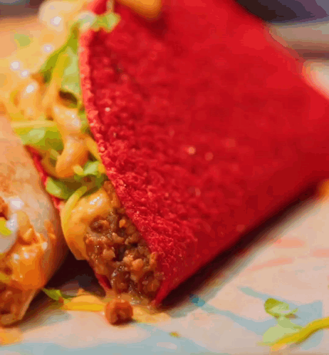 A Close Up Of A Red Taco With Meat And Cheese On A Plate GIF