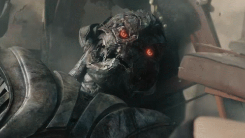 A Close Up Of A Robot With Red Eyes And The Letter T On His Chest GIF
