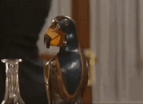 A Close Up Of A Statue Of A Parrot With A Yellow Beak On A Table . GIF