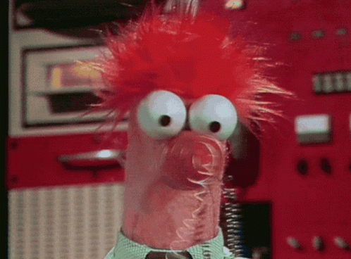 A Close Up Of A Stuffed Animal With Red Hair And Big Eyes GIF