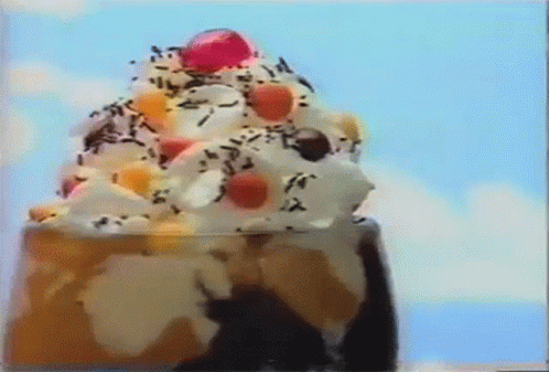 A Close Up Of A Sundae With Whipped Cream , Sprinkles , And A Cherry On Top . GIF
