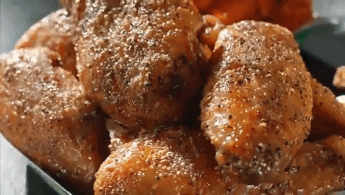 A Close Up Of A Tray Of Chicken Wings With Pepper On Them GIF