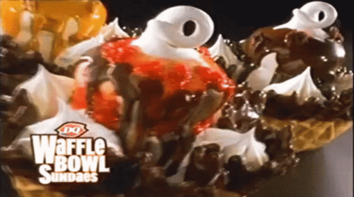 A Close Up Of A Waffle Bowl Sundae With Strawberries Chocolate And Whipped Cream GIF