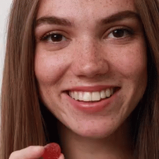 A Close Up Of A Woman Holding A Red Gummy GIF