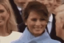 A Close Up Of A Woman In A Blue Coat Smiling In A Crowd Of People . GIF