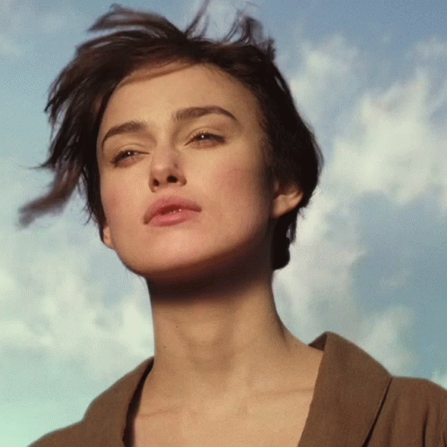 A Close Up Of A Woman 'S Face Against A Blue Sky With Clouds GIF