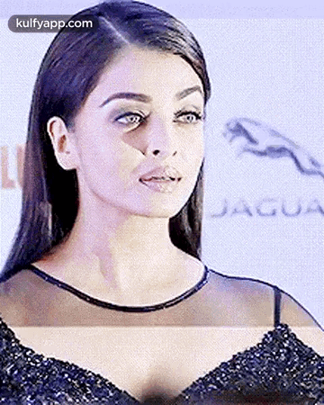 A Close Up Of A Woman 'S Face In A Black Dress With A Jaguar Logo In The Background . GIF