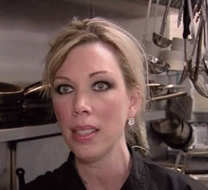 A Close Up Of A Woman 'S Face In A Kitchen With Pots And Pans Hanging From The Ceiling . GIF