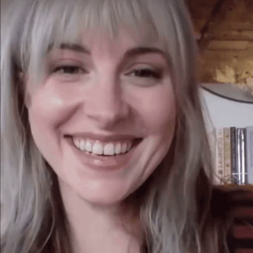 A Close Up Of A Woman 'S Face Smiling In Front Of A Bookshelf Filled With Books . GIF
