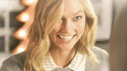 A Close Up Of A Woman 'S Face Smiling With A Christmas Tree In The Background . GIF