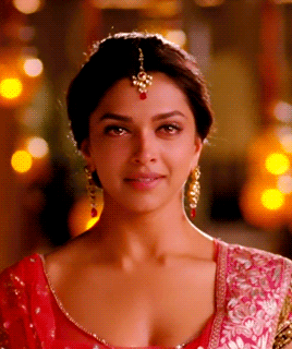 A Close Up Of A Woman 'S Face Wearing A Red Top And Gold Earrings GIF