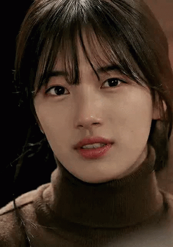 A Close Up Of A Woman 'S Face Wearing A Turtleneck Sweater And Looking At The Camera . GIF