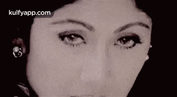 A Close Up Of A Woman 'S Face Wearing Earrings And Looking At The Camera . GIF