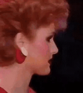 A Close Up Of A Woman 'S Face Wearing Red Earrings And Red Hair . GIF