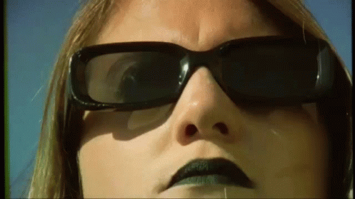 A Close Up Of A Woman 'S Face Wearing Sunglasses And Black Lipstick . GIF