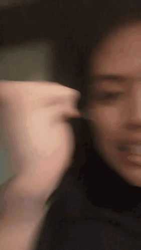 A Close Up Of A Woman 'S Face With A Blurry Background And A Hand Behind Her Ear . GIF
