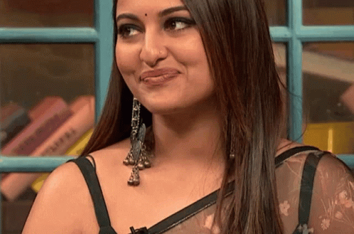 A Close Up Of A Woman 'S Face With A Bookshelf In The Background GIF