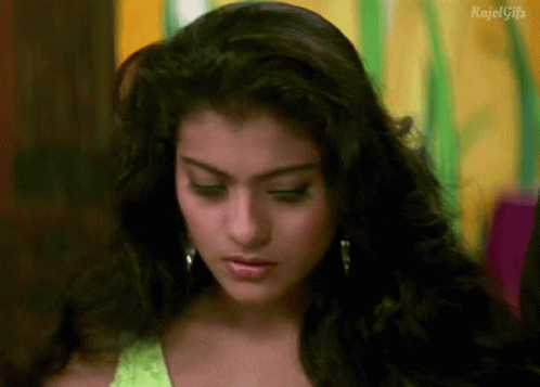 A Close Up Of A Woman 'S Face With A Green Top And Earrings . GIF