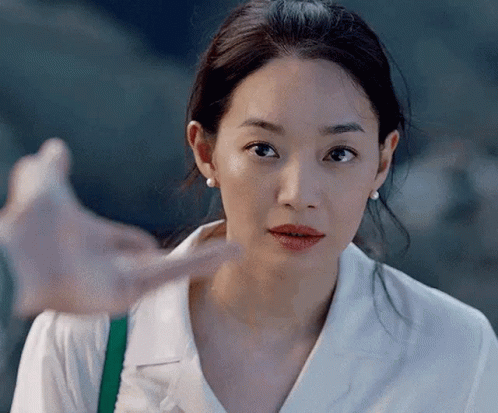 A Close Up Of A Woman 'S Face With A Hand Pointing To Her Face . GIF
