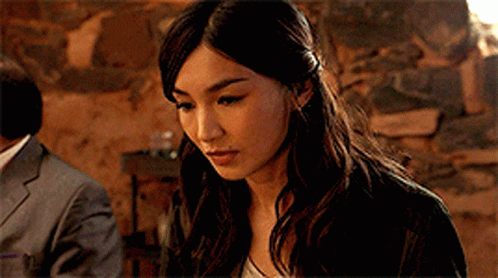 A Close Up Of A Woman 'S Face With A Man In A Suit In The Background GIF