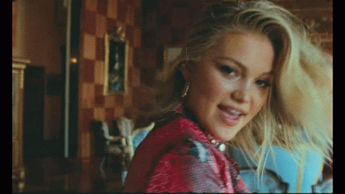 A Close Up Of A Woman 'S Face With A Picture In The Background GIF